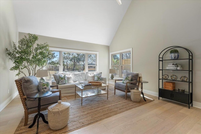 living room with baseboards, high vaulted ceiling, and light wood finished floors