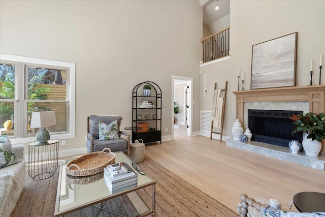 living room featuring light wood-style flooring, a fireplace, a high ceiling, and baseboards