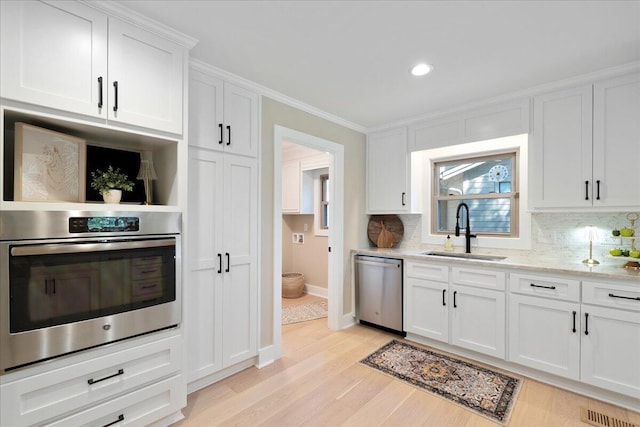 kitchen featuring a sink, tasteful backsplash, stainless steel appliances, light wood-style floors, and white cabinets