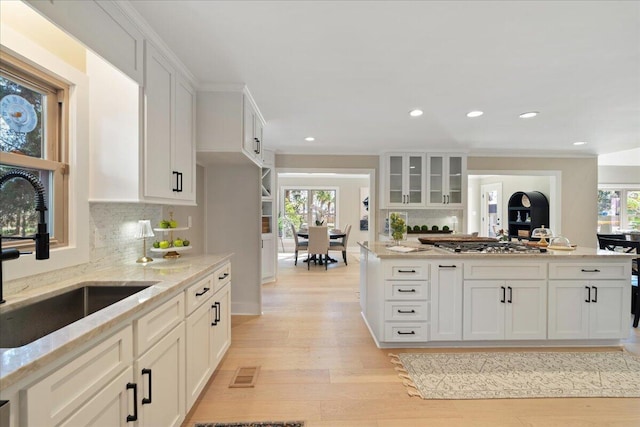 kitchen with a sink, light stone counters, plenty of natural light, white cabinetry, and light wood-style floors