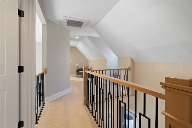 corridor featuring visible vents, baseboards, lofted ceiling, light wood-style flooring, and an upstairs landing