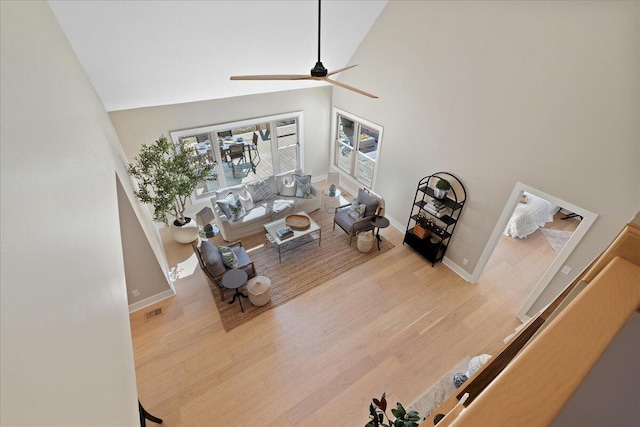 living room featuring wood finished floors, visible vents, baseboards, high vaulted ceiling, and ceiling fan