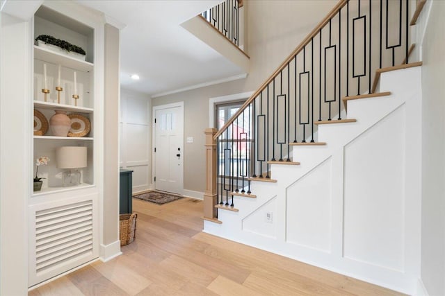 foyer featuring baseboards, light wood-style flooring, recessed lighting, stairs, and crown molding