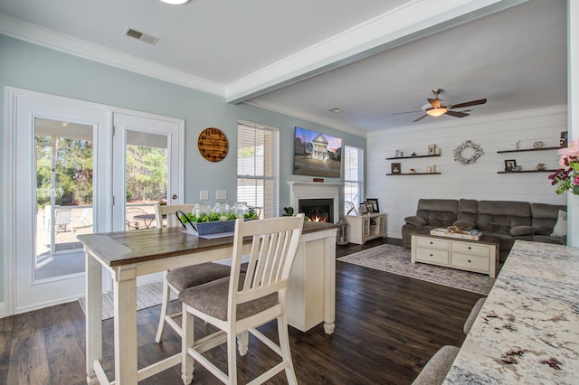 dining room with dark wood-style floors, a lit fireplace, ornamental molding, and visible vents