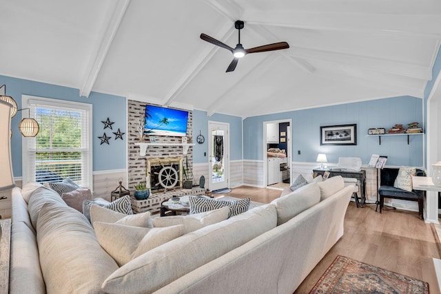 living area with wood finished floors, a brick fireplace, a ceiling fan, and wainscoting