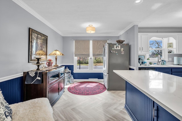 kitchen with a sink, freestanding refrigerator, blue cabinets, and ornamental molding