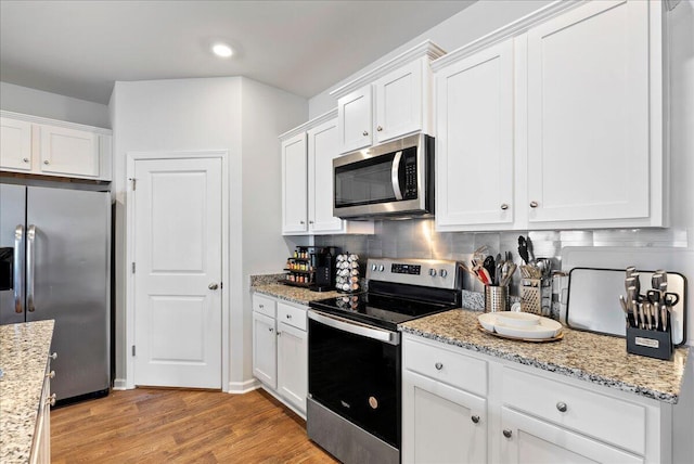 kitchen featuring decorative backsplash, light wood-type flooring, stainless steel appliances, white cabinets, and light stone counters