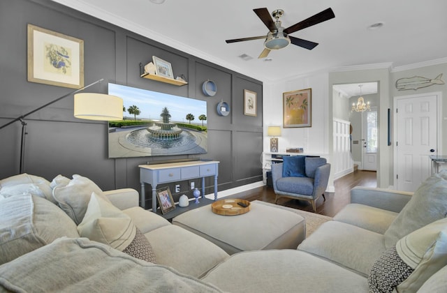 living area featuring ceiling fan with notable chandelier, crown molding, a decorative wall, and wood finished floors