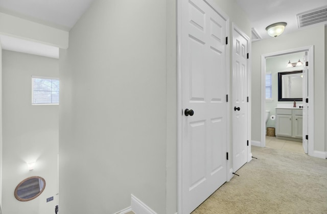 hallway with baseboards, visible vents, and light carpet