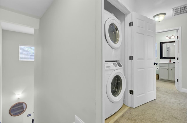 laundry area with visible vents, light carpet, a sink, stacked washing maching and dryer, and laundry area