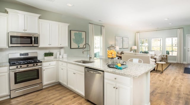 kitchen with appliances with stainless steel finishes, a sink, a peninsula, light wood-type flooring, and white cabinetry