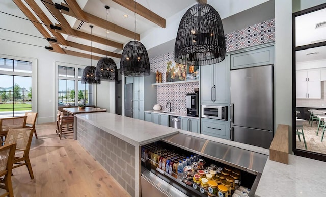 kitchen featuring stainless steel appliances, a sink, beamed ceiling, a chandelier, and tasteful backsplash