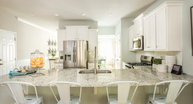kitchen with stainless steel appliances, light stone countertops, a sink, a peninsula, and recessed lighting