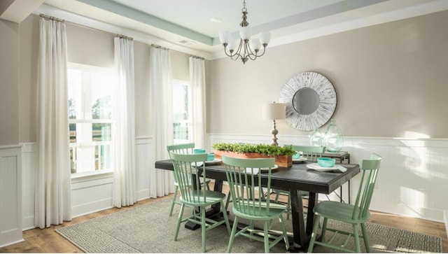 dining space with wainscoting, a chandelier, wood finished floors, a decorative wall, and a raised ceiling