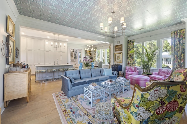 living room with ornamental molding, an ornate ceiling, light wood-type flooring, a chandelier, and bar area