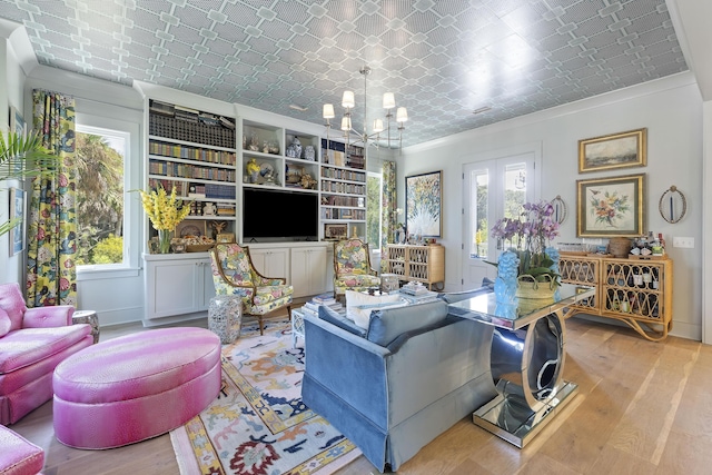 living area featuring wood finished floors, crown molding, an ornate ceiling, and a chandelier