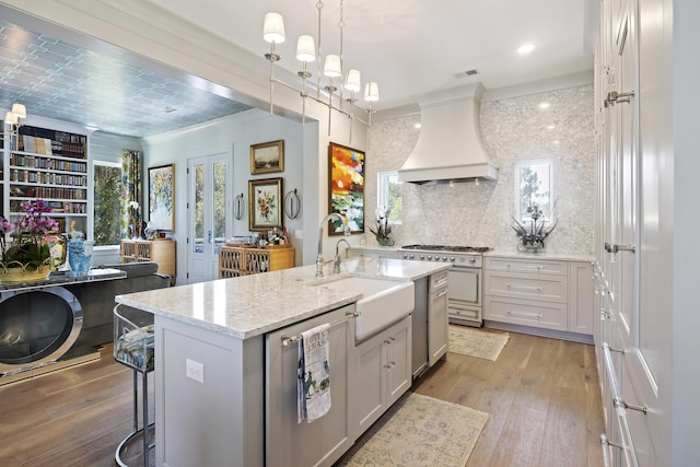 kitchen with a sink, appliances with stainless steel finishes, custom exhaust hood, and light wood-style flooring