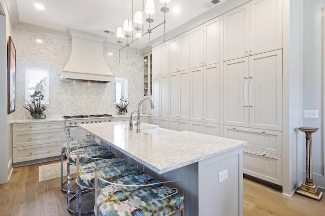 kitchen with a kitchen bar, tasteful backsplash, a sink, custom range hood, and light wood-style flooring