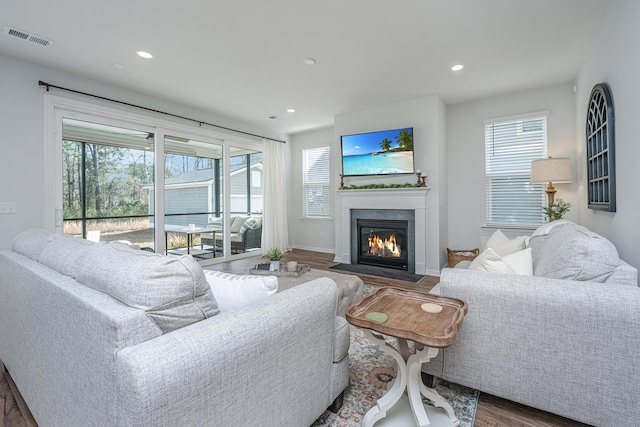 living area featuring a healthy amount of sunlight, a fireplace with flush hearth, visible vents, and wood finished floors