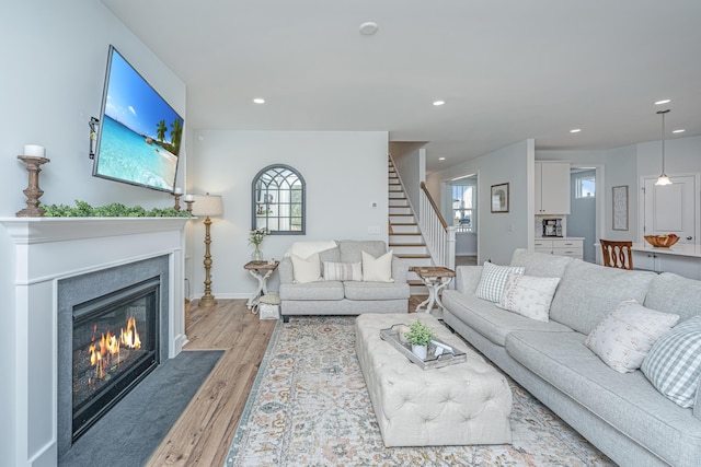 living room with recessed lighting, light wood-style flooring, a fireplace with flush hearth, baseboards, and stairs