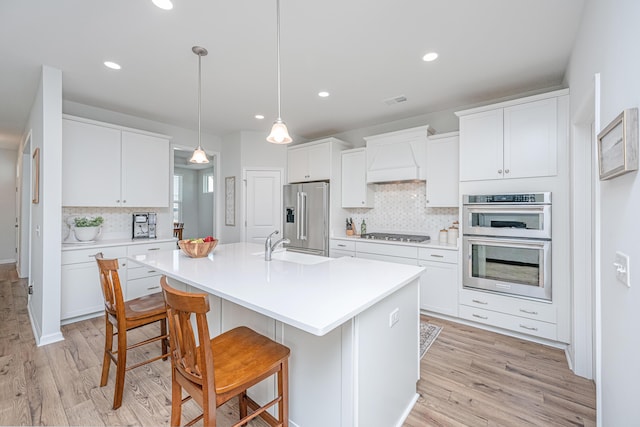 kitchen featuring appliances with stainless steel finishes, light wood-type flooring, premium range hood, and a sink