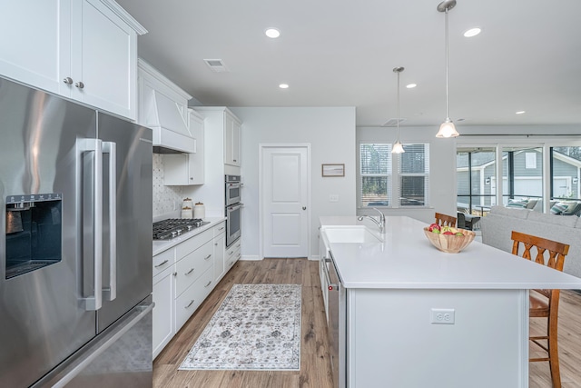 kitchen featuring light wood finished floors, visible vents, a breakfast bar, stainless steel appliances, and a sink