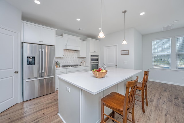 kitchen with light wood finished floors, visible vents, custom range hood, decorative backsplash, and appliances with stainless steel finishes