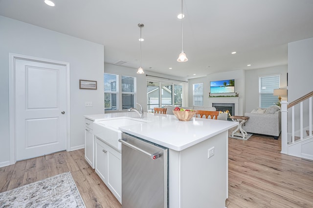 kitchen with a center island with sink, dishwasher, light wood-style flooring, a lit fireplace, and white cabinetry