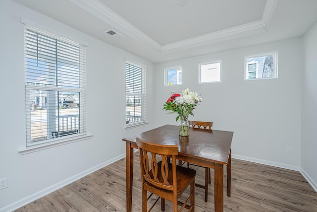 dining room with a tray ceiling, visible vents, crown molding, and light wood-style flooring