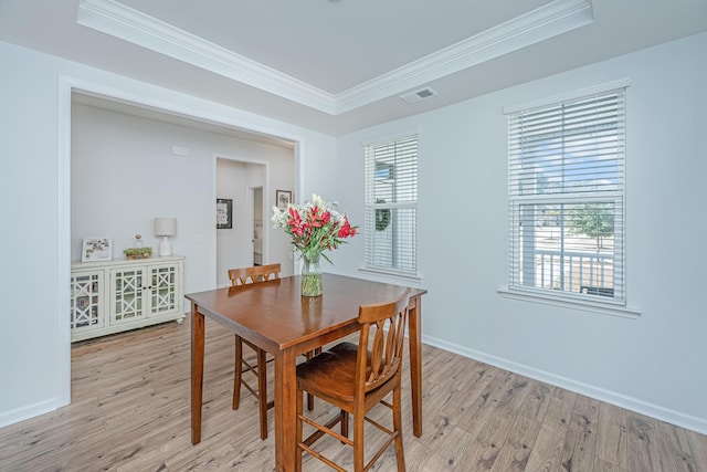 dining space featuring a tray ceiling, light wood-style flooring, visible vents, and crown molding