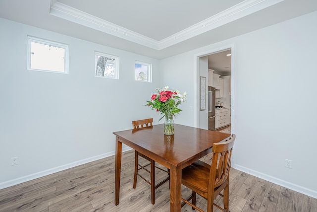 dining room featuring light wood finished floors, a tray ceiling, ornamental molding, and baseboards