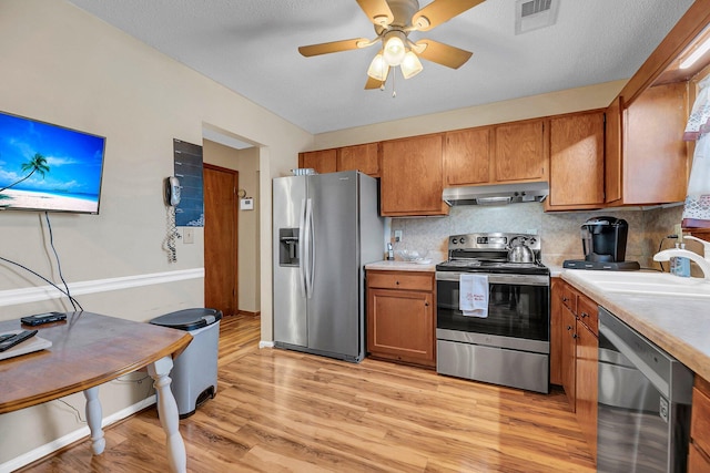 kitchen featuring decorative backsplash, appliances with stainless steel finishes, ceiling fan, sink, and light hardwood / wood-style flooring