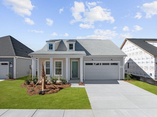 view of front of house with a shingled roof, covered porch, an attached garage, a front yard, and driveway