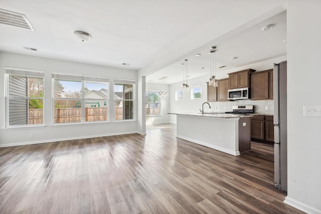 kitchen featuring stainless steel appliances, a sink, visible vents, open floor plan, and decorative backsplash