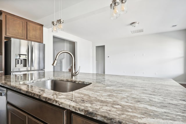 kitchen featuring light stone counters, stainless steel appliances, a sink, visible vents, and decorative light fixtures