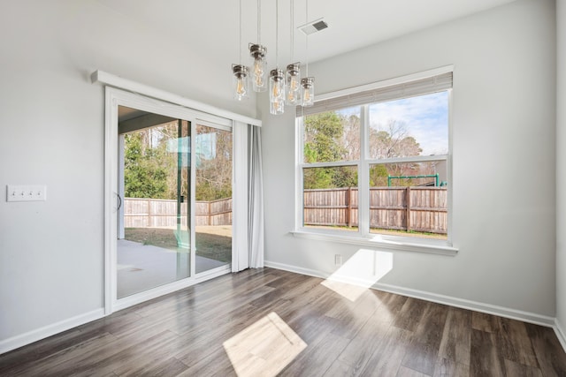 unfurnished dining area with an inviting chandelier, visible vents, baseboards, and wood finished floors