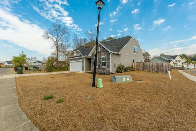 view of front of house with an attached garage, stone siding, concrete driveway, and fence