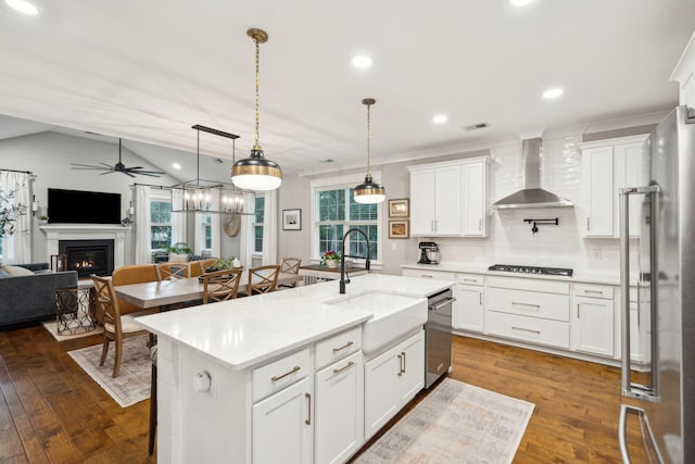 kitchen with white cabinets, sink, an island with sink, and wall chimney range hood