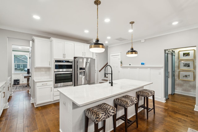 kitchen featuring appliances with stainless steel finishes, decorative light fixtures, white cabinetry, and an island with sink