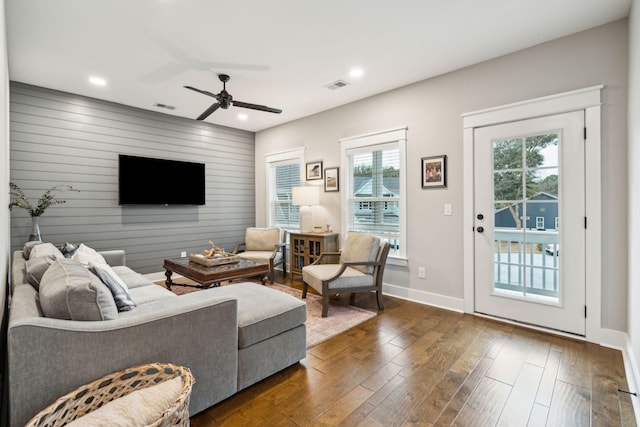 living room with ceiling fan, dark hardwood / wood-style flooring, and wood walls