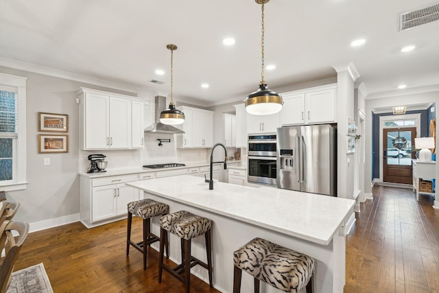 kitchen featuring backsplash, stainless steel appliances, wall chimney range hood, white cabinetry, and a breakfast bar area