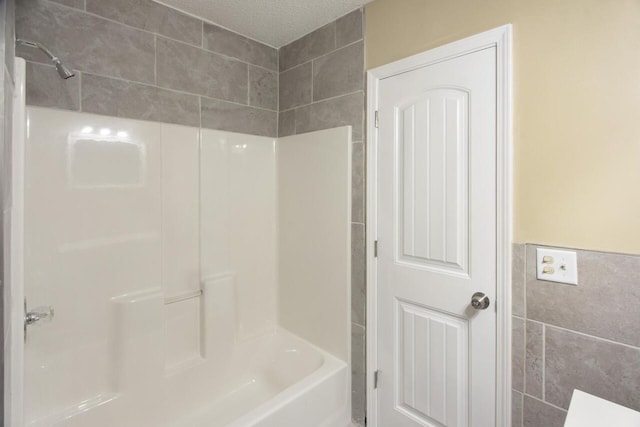 bathroom featuring a textured ceiling, tile walls, and bathing tub / shower combination