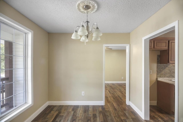 spare room with a notable chandelier, a textured ceiling, and dark wood-type flooring