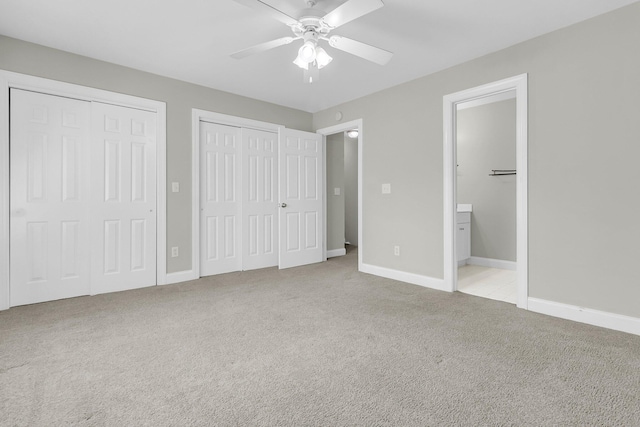 unfurnished bedroom featuring ceiling fan, ensuite bathroom, light colored carpet, and multiple closets