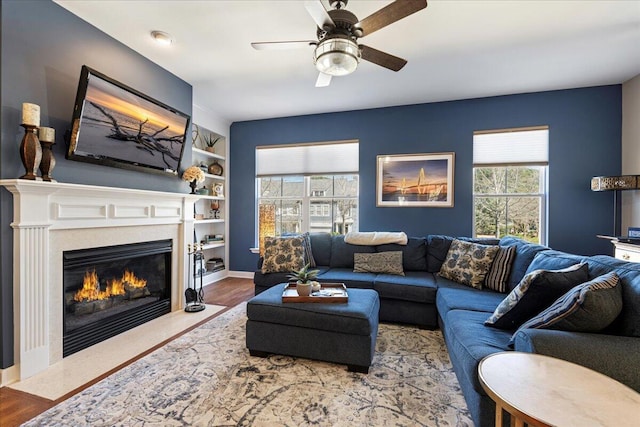 living room with a fireplace with flush hearth, a ceiling fan, built in features, and wood finished floors