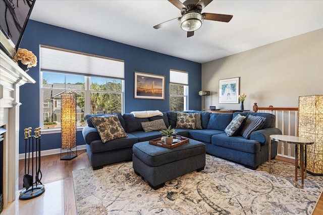 living room featuring ceiling fan, a fireplace, wood finished floors, and baseboards