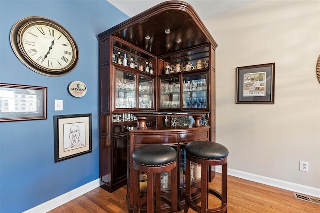 bar with a dry bar, wood finished floors, visible vents, and baseboards