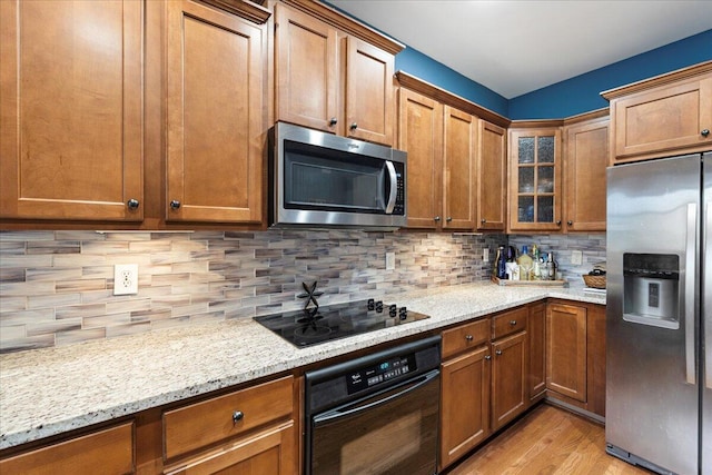 kitchen with decorative backsplash, brown cabinets, light wood finished floors, and black appliances