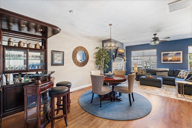 dining space featuring ceiling fan with notable chandelier, wood finished floors, visible vents, and baseboards