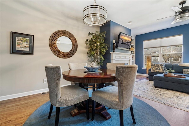 dining space with baseboards, wood finished floors, and ceiling fan with notable chandelier